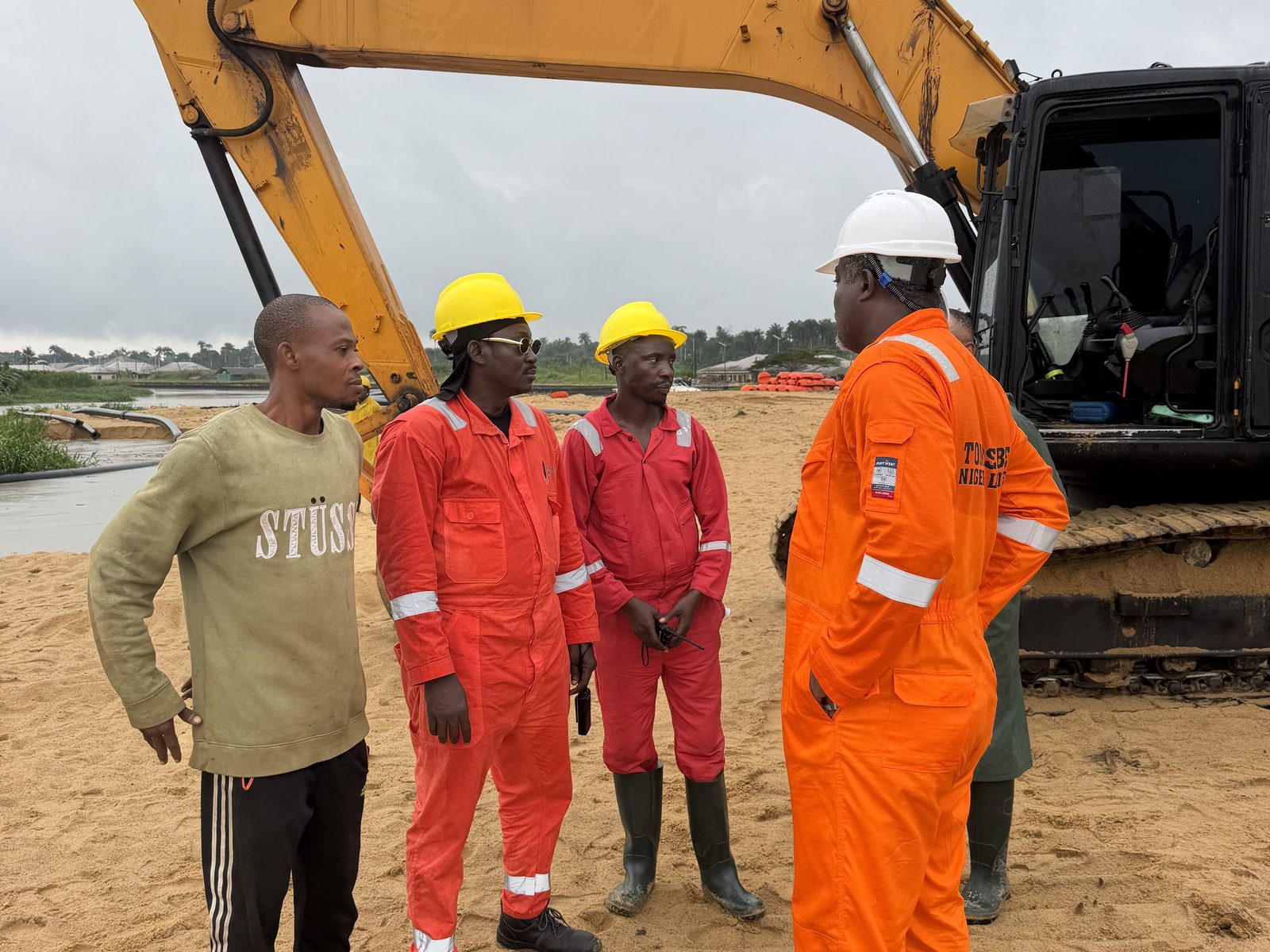 Site crew briefing beside a tracked excavator on reclaimed sand